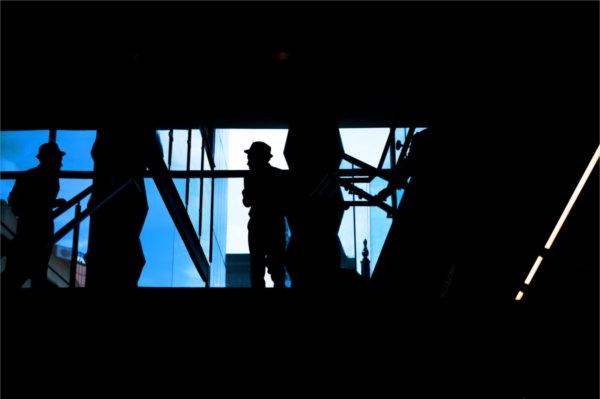   A person wearing a hat is silhouetted against a blue window. 