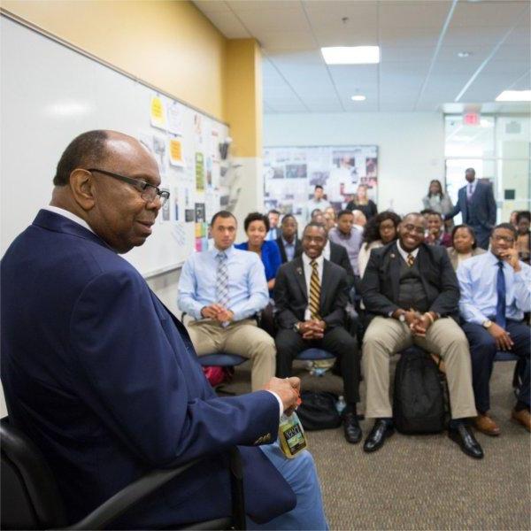 William Pickard at left seated in chair, rows of students listening in the Multicultural Affairs office