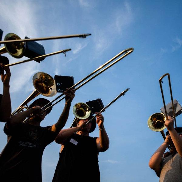 A group of people playing trombones is seen from ground level.